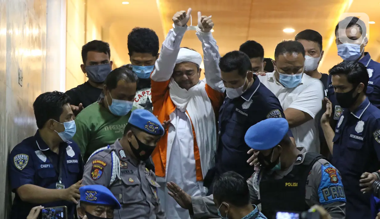M Rizieq Shihab (tengah) digiring petugas saat meninggalkan gedung Ditreskrimum Polda Metro Jaya, Jakarta, Minggu dini hari (13/12/2020). Rizieq Shihab ditahan setelah menjalani pemeriksaan sebagai tersangka penghasutan dan kerumunan di tengah pandemi COVID-19. (Liputan6.com/Helmi Fithriansyah)