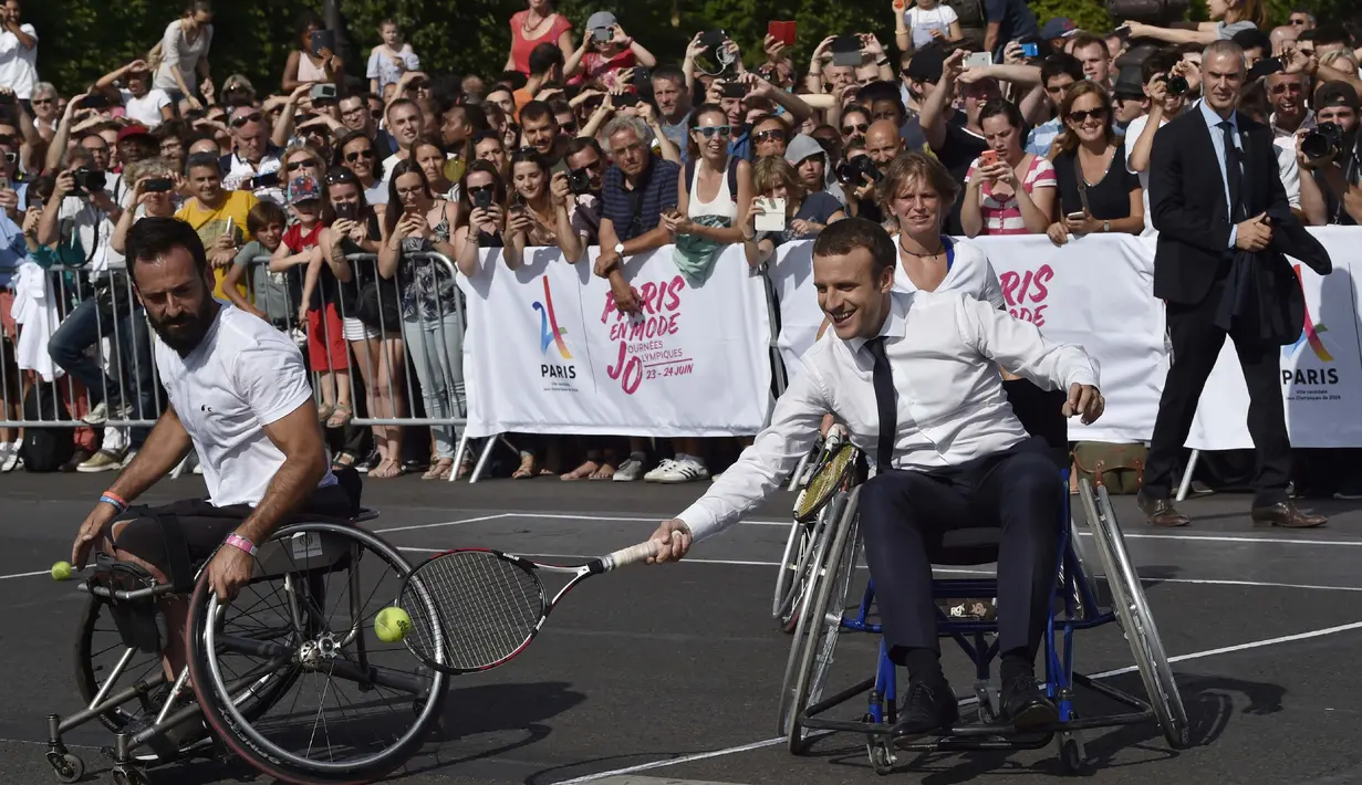 Presiden Prancis, Emmanuel Macron (tengah) bermain tenis menggunakan kursi roda bersama atlet, Michael Jeremiasz (kiri) di Paris, (24/6/2017). Kegiatan ini sebagai bentuk promosi Paris menjadi kandidat tuan rumah Olimpiade 2024. (AFP/Alain Jocard)