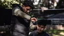 Mohammed al-Hamo (kiri) memotong rambut saudara laki-lakinya, Sobhi di depan tenda mereka di kamp darurat pengungsi korban gempa Turki dan Suriah di kota Antakya pada 19 Februari 2023. Hamo berhasil mengambil gunting listrik, sisir, gunting, dan sampo dari reruntuhan rumahnya yang hancur. (Sameer Al-DOUMY / AFP)