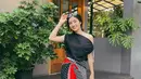 Febby Rastanty mengenakan atasan one shoulder warna hitam, dipadukan kain lilit didominasi warna hitam dan merah dan sepatu Adidas Samba putihnya. [@febbyrastanty]