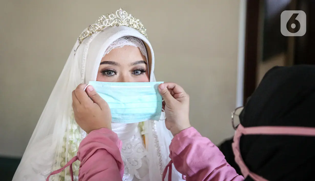 Pengantin wanita dipasangkan masker sebelum melaksanakan prosesi akad nikah di KUA Jagakarsa, Jakarta, Sabtu (6/6/2020). Pernikahan mengikuti protokol kesehatan sesuai Surat Edaran (SE) Menteri Agama Nomor 15 Tahun 2020. (Liputan6.com/Faizal Fanani)