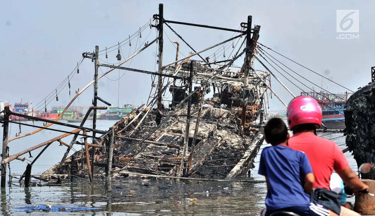 Pengendara sepeda motor melintas dekat kapal yang ludes dilalap api di Pelabuhan Muara Baru, Jakarta, Minggu (24/2). Sebanyak 18 unit kapal tradisional hangus akibat kebakaran pada Sabtu, 23 Februari 2019. (Merdeka.com/Iqbal Nugroho)