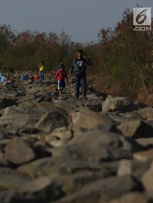 Warga berjalan di bibir pantai saat sore hari di Pantai Marunda, Teluk Jakarta, Selasa (11/9). Pantai Marunda menjadi tempat alternatif berlibur keluarga dan menghibur diri dengan memancing di bibir pantai tersebut. (Merdeka.com/Imam Buhori)
