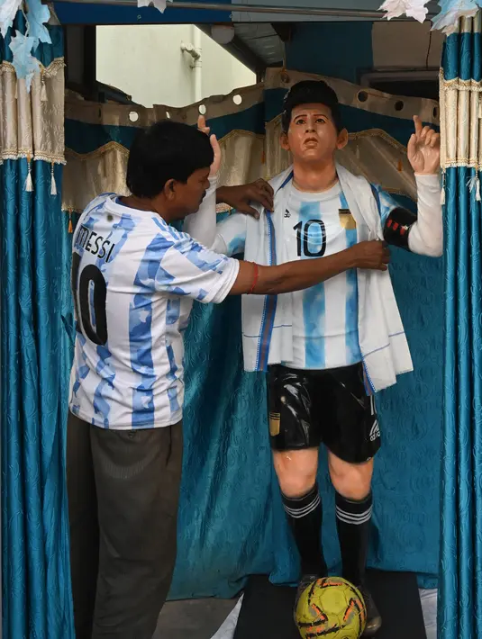 Fans Argentina Shib Shankar Patra menyesuaikan patung Lionel Messi yang dipasang di samping kedai tehnya yang dicat dengan warna tim, di Ichhapur sekitar 35 km sebelah utara Kolkata pada 12 Desember 2022. Argentina berhasil lolos ke babak semifinal Piala Dunia 2022 Qatar yang akan melawan Kroasia. (AFP/Dibyangshu Sarkar)