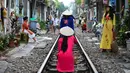 Turis mengenakan kostum tradisional Vietnam berfoto di tengah jalur kereta api yang melintasi kawasan permukiman di Hanoi, 20 Oktober 2018. Rel kereta ini menjadi titik bagi wisatawan untuk berfoto dan mengunggahnya di jejaring sosial. (Nhac NGUYEN/AFP)