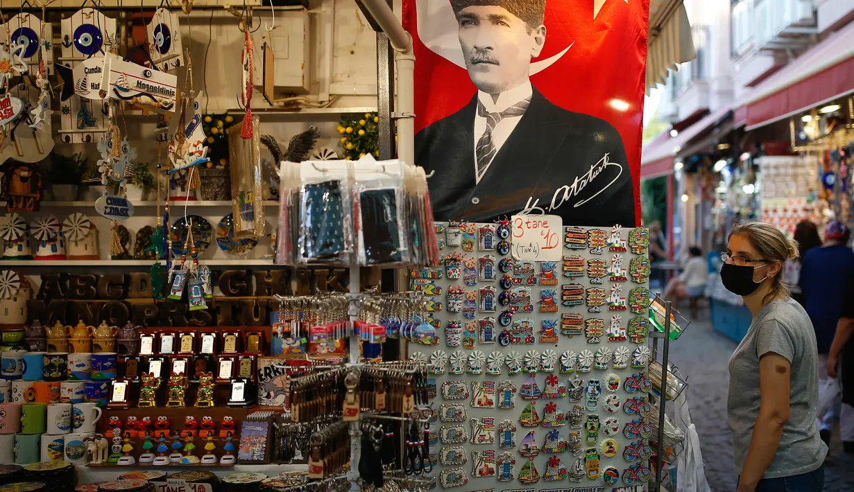 Poster pendiri Turki modern Mustafa Kemal Ataturk terlihat di sebuah toko, ketika turis yang mengenakan masker melintas di kota Ayvalik, Laut Aegea, Rabu (9/9/2020). Turki telah mewajibkan penggunaan masker di semua lokasi selain di rumah, menyusul lonjakan kasus COVID-19. (AP Photo/Emrah Gurel)