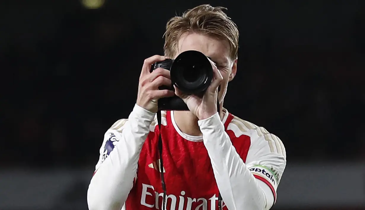 Pemain Arsenal, Martin Odegaard merayakan kemenangan dengan menjadi seorang fotografer setelah laga lanjutan Liga Inggris 2023/2024 melawan Liverpool di Emirates Stadium, London, Inggris, Minggu (05/02/2024) WIB. (AFP/Ian Kington)