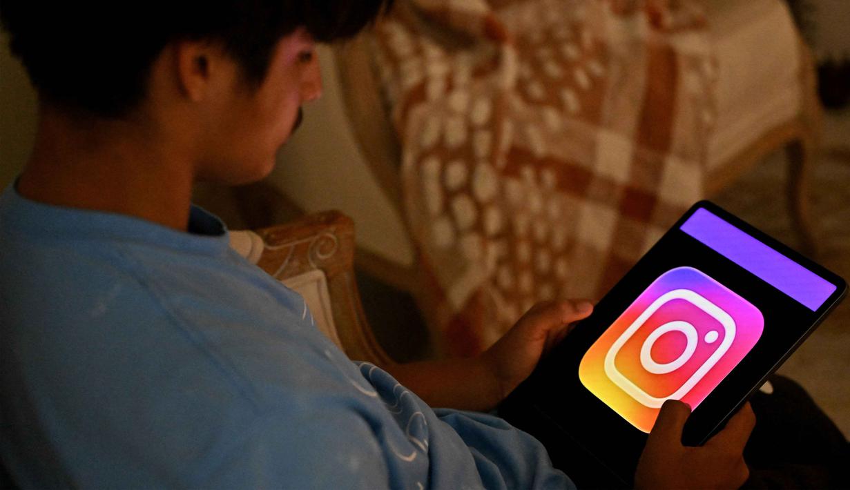 Larangan ini bersifat tegas, disertai sanksi denda hingga AUD 49,5 juta atau sekitar Rp 544 miliar bagi platform yang melanggar sejak aturan diberlakukan mulai 10 Desember 2025. Tampak dalam foto, seorang anak laki-laki berusia 13 tahun berpose di rumahnya sambil melihat media sosial di tabletnya di Sydney, Australia pada Senin 8 Desember 2025. (Saeed KHAN/AFP)