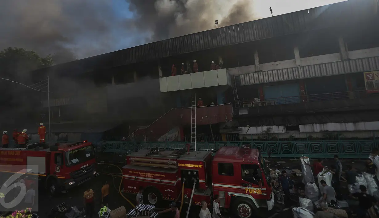 Petugas pemadam kebakaran berusaha memadamkan api sementara sejumlah pedagang terlihat sibuk menyelamatkan barang dagangan mereka yang masih ada di dalam Pasar Senen, Jakarta Pusat, Kamis (19/1). (Liputan6.com/Faizal Fanani)