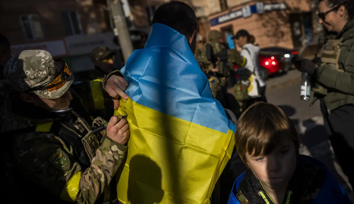 Seorang anggota pasukan pertahanan Ukraina menandatangani bendera Ukraina untuk seorang penduduk di Kherson, Ukraina selatan, Senin (14/11/2022). Penduduk Kota Kherson dengan gembira menyambut pasukan Ukraina, setelah Rusia mengatakan telah menarik diri sepenuhnya dari kota di selatan itu. (AP Photo/Bernat Armangue)