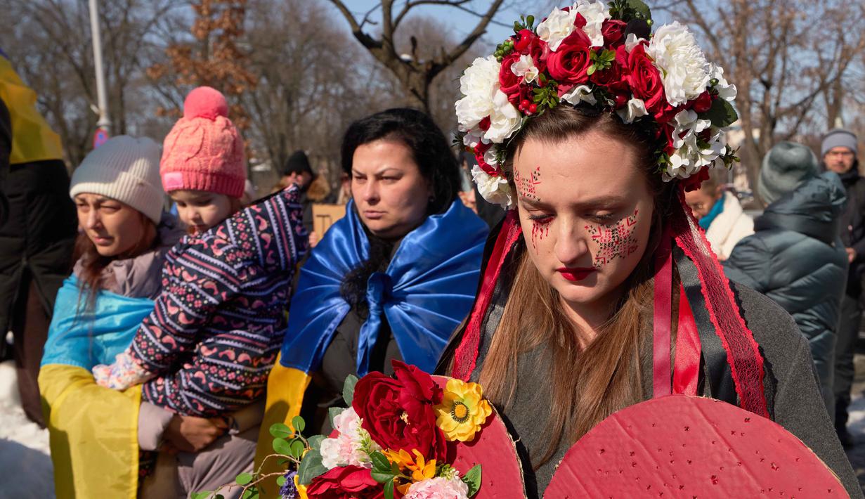 Sepanjang empat tahun, bara perang Rusia-Ukraina tak kunjung padam, korban terus berjatuhan. Tampak dalam foto, seorang wanita mengenakan mahkota bunga saat anggota komunitas Ukraina menggelar protes untuk menandai tahun keempat sejak dimulainya invasi skala penuh Rusia ke Ukraina di Bukares, Rumania, Minggu 22 Februari 2026. (AP Photo/Vadim Ghirda)