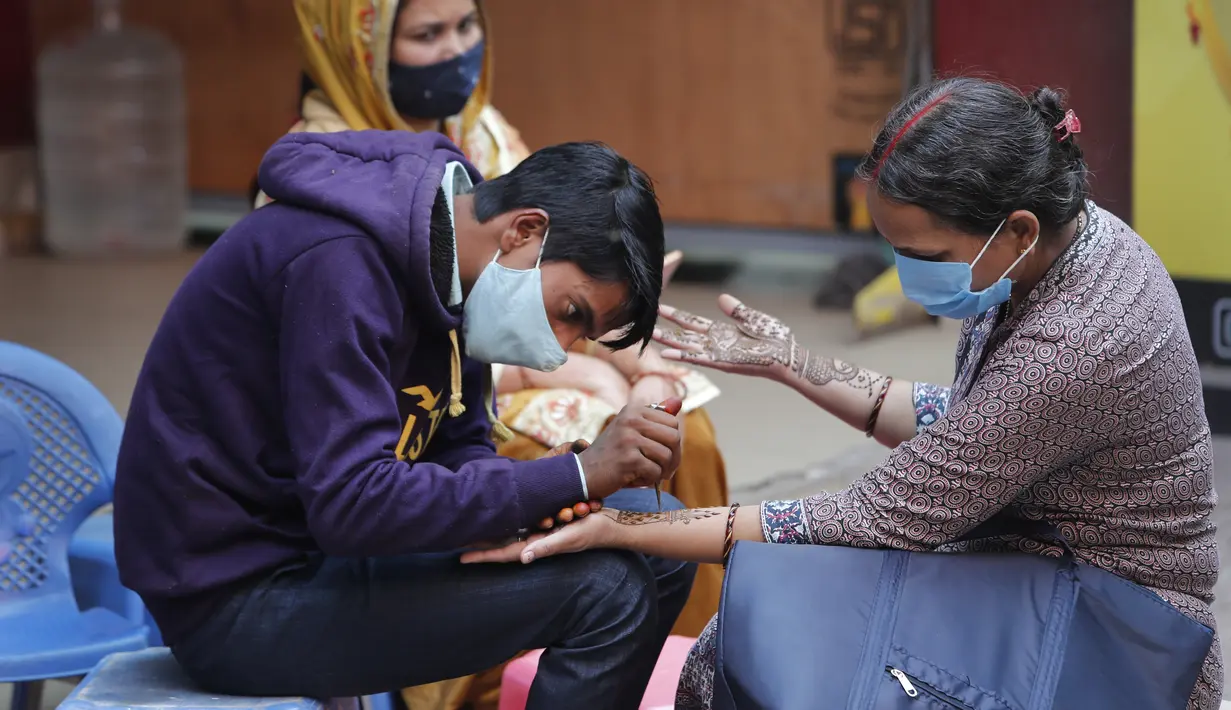 Perempuan yang mengenakan masker mendapatkan desain henna di tangan mereka pada malam festival Karva Chauth di New Delhi, India, Selasa (3/11/2020). Ini adalah festival untuk memulai bulan baru di bulan November di mana para istri akan berpuasa untuk suami-suami mereka. (AP Photo/Manish Swarup)