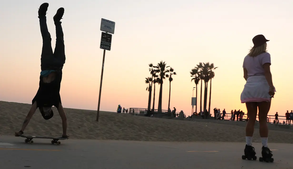 Seorang perempuan mengenakan sepatu roda di dekat pemain skateboard di sepanjang Venice Beach di Venice, California, Kamis (3/9/2020). Permintaan sepatu roda di Amerika Serikat mengalami peningkatan tajam di tengah pembatasan sosial akibat corona Covid-19. (Mario Tama/Getty Images/AFP)