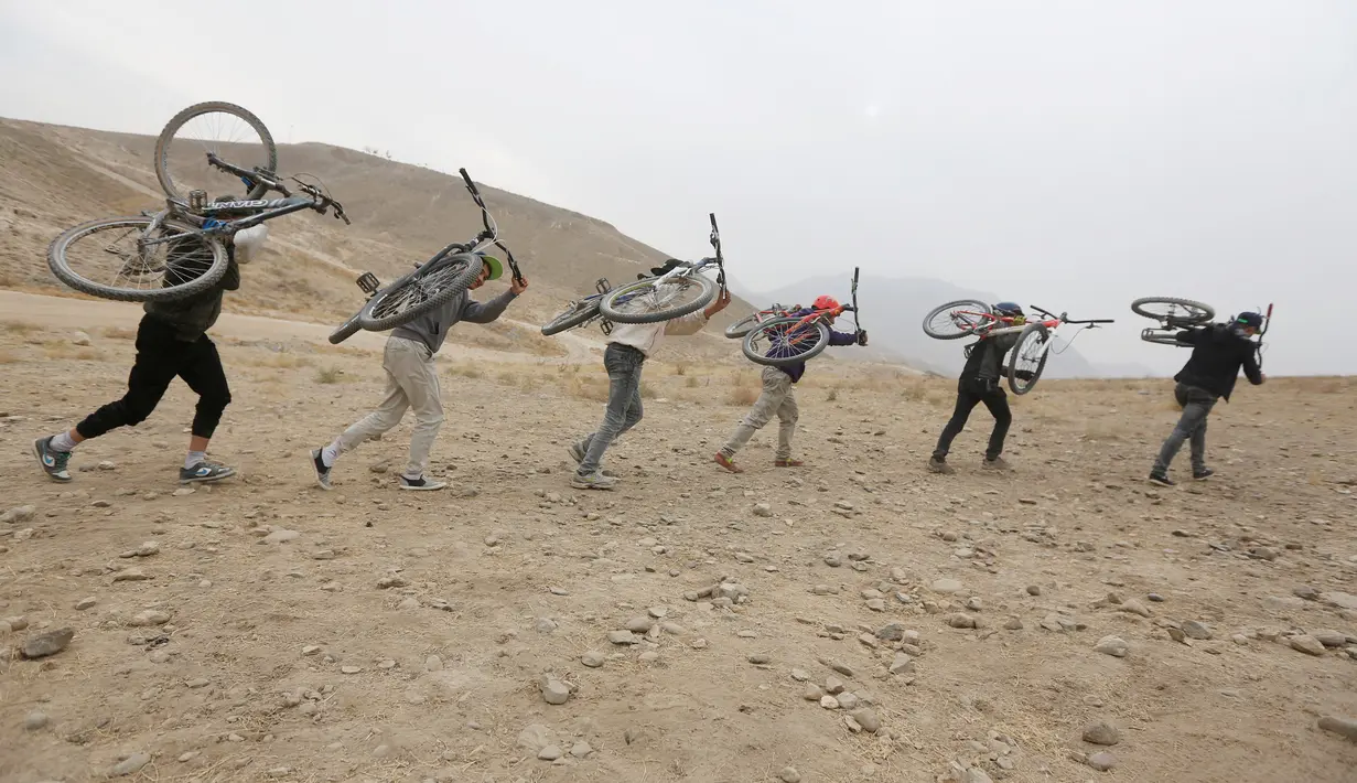 Sejumlah pemuda Afghanistan mengangkat sepedanya menaiki bukit saat berlatih Dirt Jump (DJ) di Kabul, Afghanistan (20/11). Sepeda Dirt Jump memiliki setang yang mirip dengan BMX tetapi frame lebih besar. (Reuters/Omar Sobhani)
