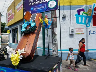 Warga berjalan dekat peti mati dengan tulisan, "Anda memutuskan, di rumah atau di dalam kotak ini", sebagai bagian dari kampanye pemerintah setempat di jalan-jalan kotamadya Escuintla, Guatemala City pada 21 Juli 2020. Kampanye itu sebagai upaya menghentikan penyebaran COVID-19. (Johan ORDONEZ/AFP)
