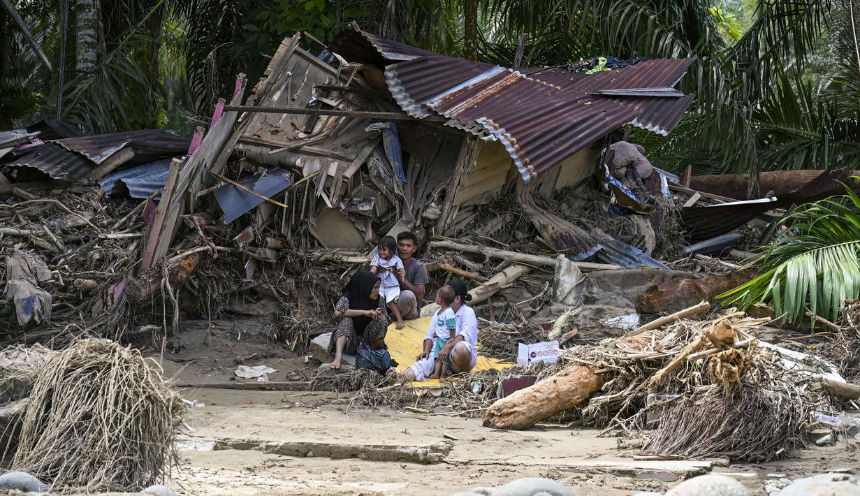 Kerusakan juga terjadi pada fasilitas umum lainnya, seperti jembatan dan akses jalan, yang mengganggu mobilitas dan menyebabkan beberapa wilayah terisolasi sementara. Tampak dalam foto, warga desa duduk di luar rumah mereka yang rusak akibat banjir bandang di Garoga, Provinsi Sumatera Utara, pada Kamis 4 Desember 2025. (YT HARIONO/AFP)