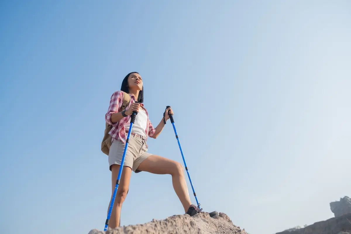 Seorang perempuan berdiri di atas sebuah gunung dengan memegang dua tongkat tracking (Foto Dok: Freepik/jcomp)