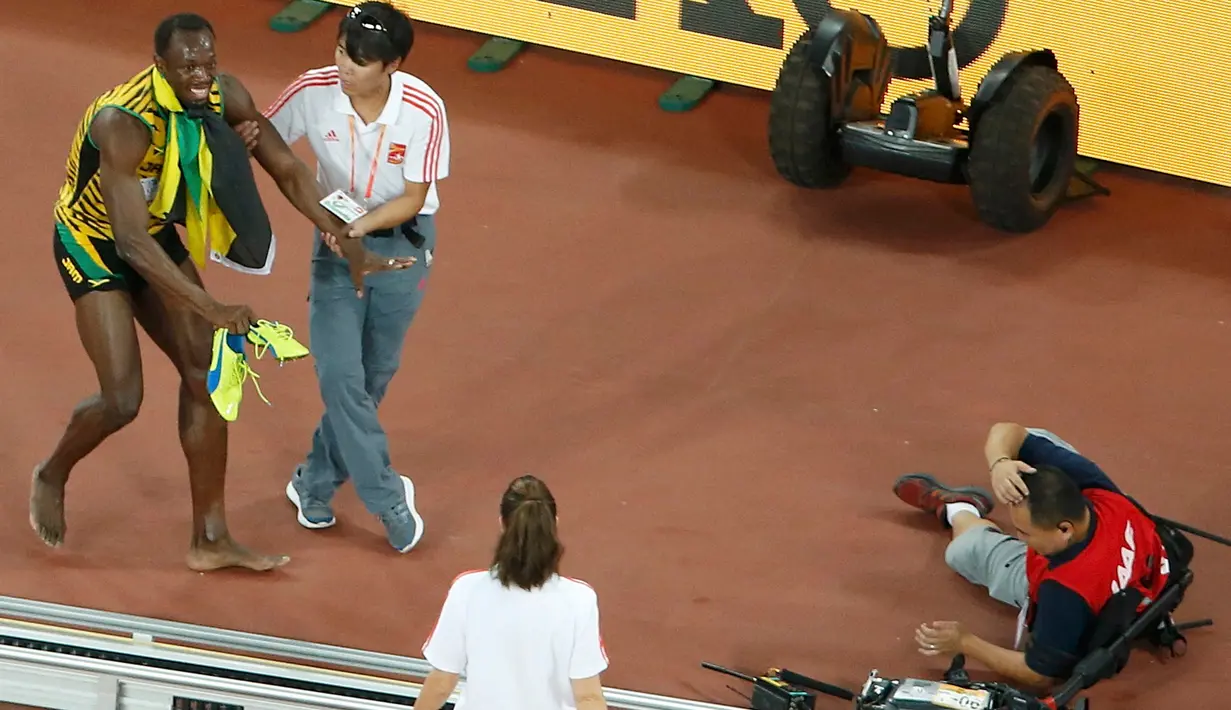 Dibantu petugas, pelari Jamaika, Usain Bolt berdiri menahan sakit usai tertabrak kameramen yang mengendarai skuter saat melakukan selebrasi kemenangan di nomor 200 meter pada Kejuaran Dunia Atletik di Beijing, Kamis (27/8). (REUTERS/Kim Kyung-Hoon)