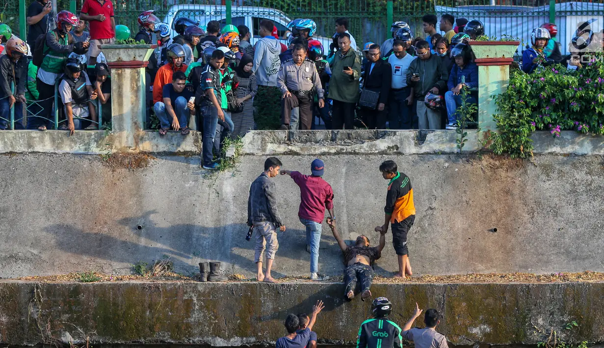 Polisi dan warga mengamankan terduga pelaku pelecehan seksual yang menceburkan diri di Kali Ciliwung, Manggarai, Jakarta, Minggu (7/6/2019). 
Pelaku menceburkan diri dan pura-pura pingsan saat dikejar massa dengan modus mencegat korban perempuan mendapat hadiah. (Liputan6.com/Fery Pradolo)