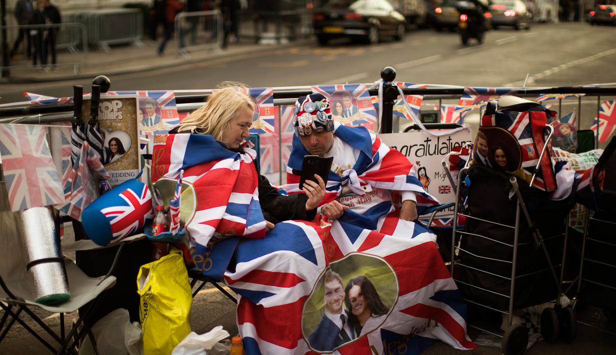 Dua penggemar Kerajaan Inggris duduk di luar Istana Windsor menjelang pernikahan Pangeran Harry dan Meghan Markle di Windsor, Inggris, (16/5). Pernikahan tersebut akan digelar pada 19 Mei 2018. (AP Photo / Emilio Morenatti)