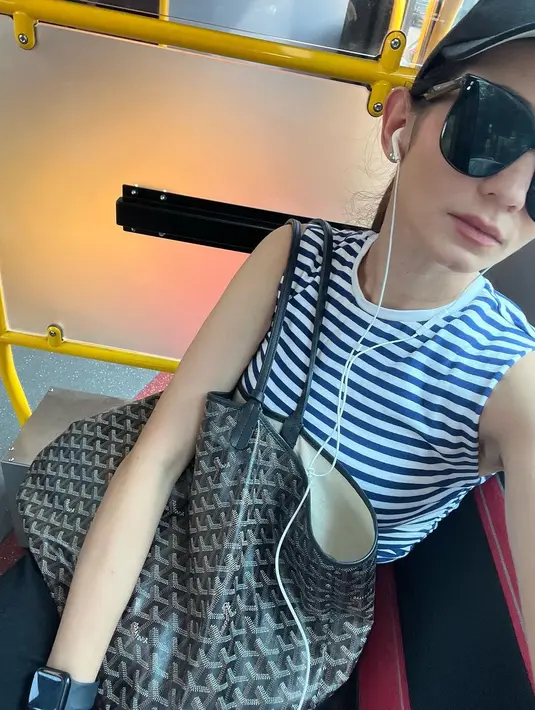 Atau momen Enzy Storia berselfie di dalam kendaraan umum. Ia mengenakan atasan tanpa lengan bermotif garis yang santai, dipadu dengan sunglasses dan topi, serta tas tote bag medium. [Foto: Instagram/enzystoria]