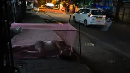 Seorang pria menggunakan jaring antinyamuk saat tidur di trotoar di New Delhi, India, Rabu (17/10). Sekitar 800 juta warga India hidup dalam kemiskinan. (AP Photo / R S Iyer)