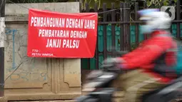 Pengendara motor melintas di depan poster protes warga terhadap pembangunan flyover di kawasan Tanjung Barat, Jakarta, Rabu (15/7/2020). Dalam poster protes tersebut, warga menuntut agar pembayaran pelunasan pembebasan lahan segera diselesaikan secara serentak. (Liputan6.com/Immanuel Antonius)