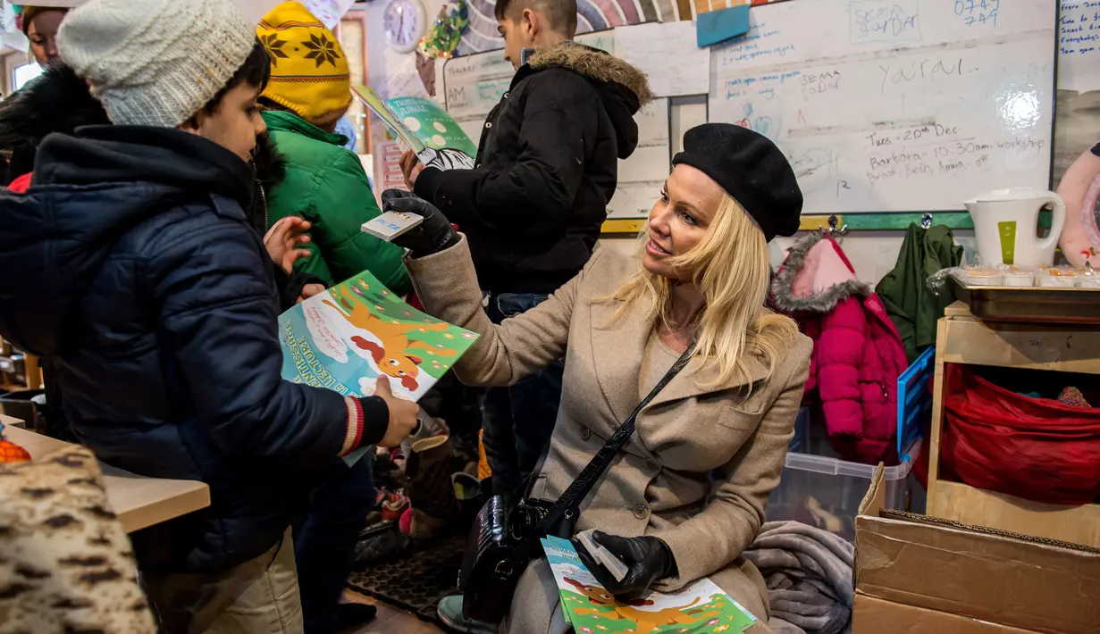 Pamela Anderson memberikan peralatan sekolah kepada seorang anak di pengungsian Grande-Synthe, Prancis (25/1). Selain itu Pamela juga bermain dan menghibur anak-anak yang berada di kamp pengungsian. (AFP/Philippe Huguen)
