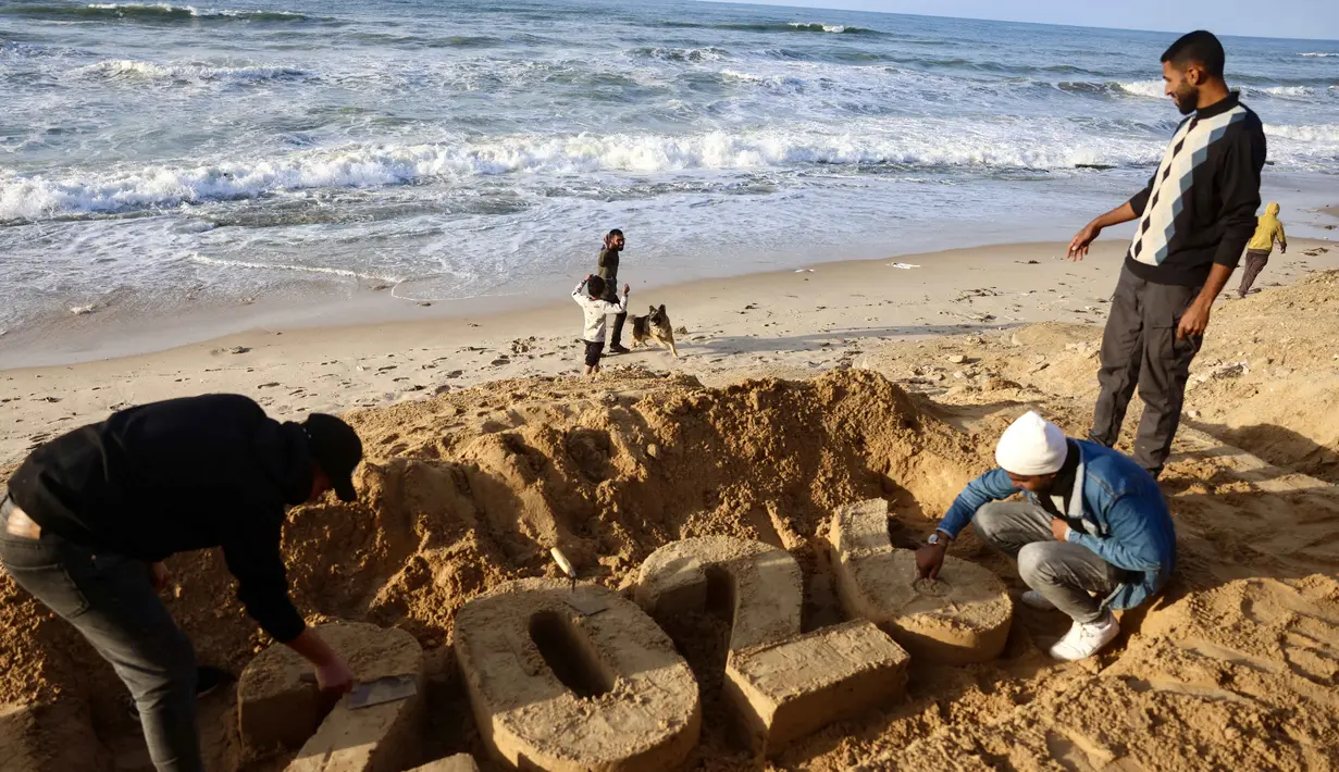 Sebagai informasi, sejak serangan Israel menghantam hampir seluruh wilayah di Gaza pada Oktober 2023 lalu, sedikitnya 71.266 orang dilaporkan tewas yang mayoritas adalah perempuan dan anak-anak. Tampak dalam foto, seniman Yazed Abo Jarad (kiri) membuat patung pasir untuk tahun mendatang di Deir El-Balah, Jalur Gaza tengah pada 30 Desember 2025. (Bashar Taleb/AFP)