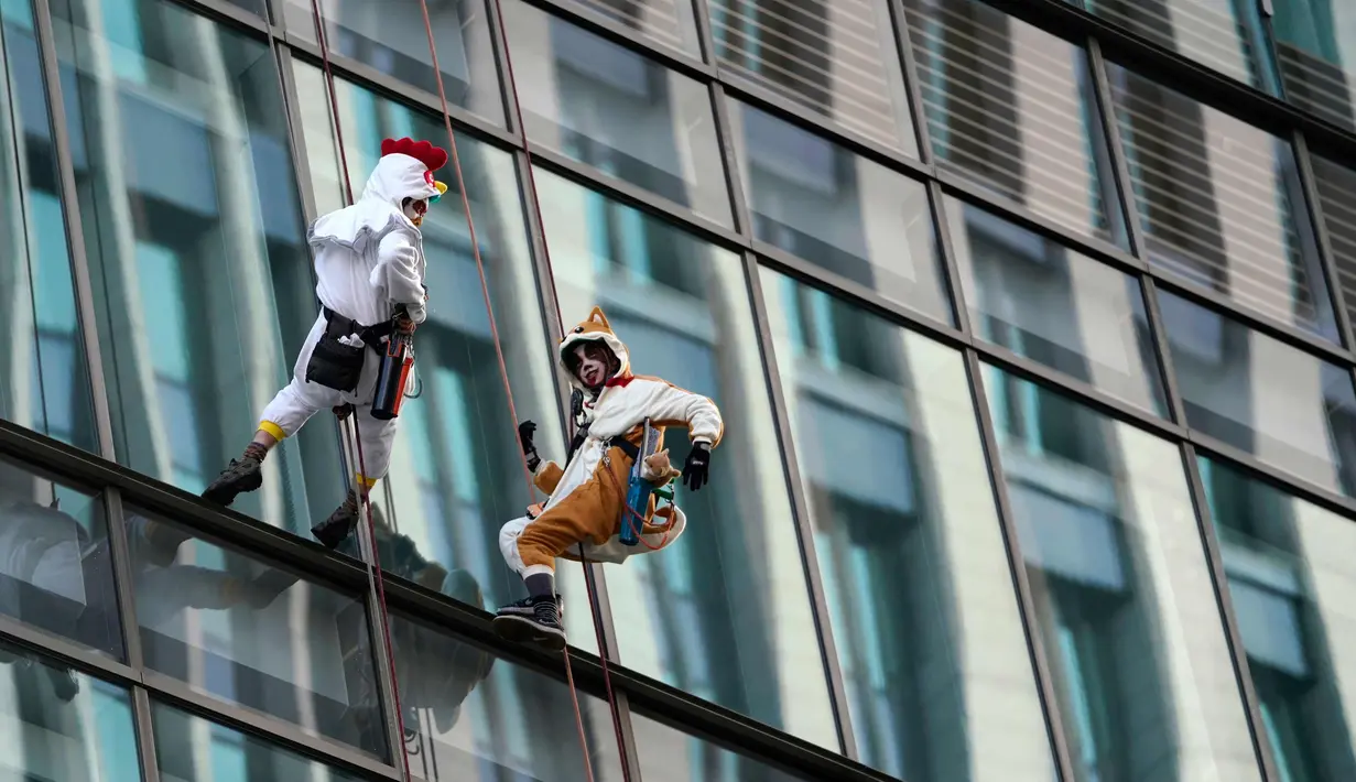 Pembersih jendela wanita berkostum ayam jago dan anjing membersihkan jendela gedung di kawasan perbelanjaan dan bisnis Tokyo, Jepang (20/12). (AP Photo / Shizuo Kambayashi)