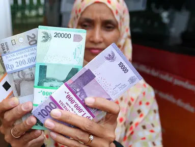 Warga menunjukkan uang kertas usai ditukarkan di penukaran uang keliling di Lapangan IRTI Monas, Jakarta, Senin (13/6). BI dan 20 bank umum lainnya membuka pelayanan penukaran uang di Monas yang dimulai 10 Juni 2016 kemarin. (Liputan6.com/Angga Yuniar)