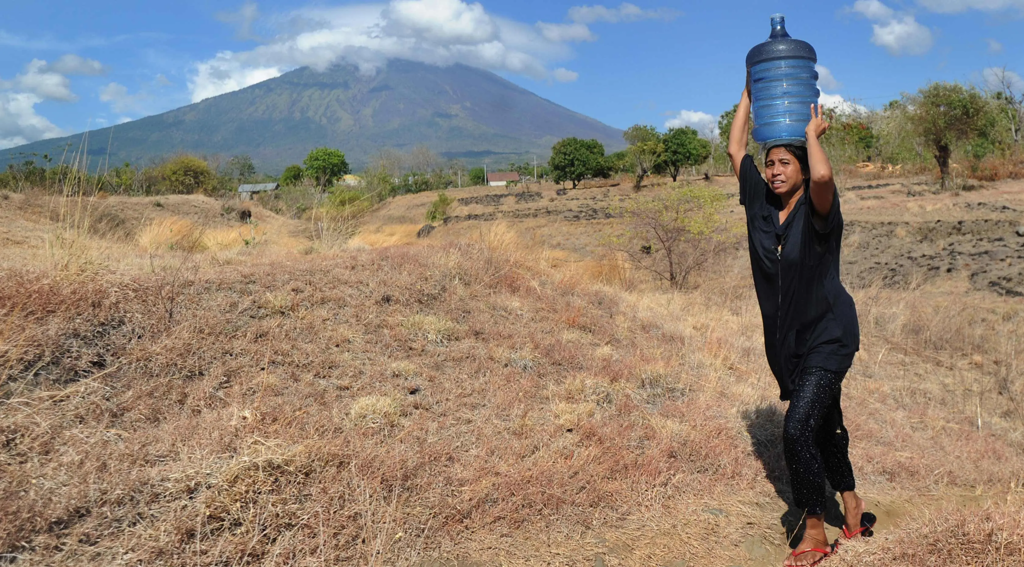 Warga membawa air melintasi perkebunan di Kec Kubu, Kab Karangasem, Bali, Selasa, (26/9). Lebih dari 57.000 orang telah mengungsi pasca peningkatan status Gunung Agung di Bali. (AP Photo / Firdia Lisnawati)