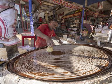 Pembuat penganan Mesir Mostafa Anwar membuat makanan penutup tradisional yang disebut "Kunafa" sebelum berbuka puasa, di kiosnya di ibu kota Kairo pada 14 April 2022.  Kunafa merupakan hidangan pencuci mulut utama di kalangan orang Arab selama Ramadhan berlangsung. (Khaled DESOUKI/AFP)