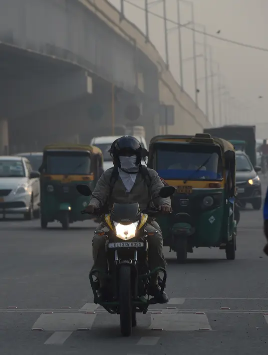 Pengendara motor mengenakan masker di tengah kondisi kabut asap tebal di New Delhi (30/10). Tingkat kabut melonjak selama musim dingin di Delhi, ketika kualitas udara sering melampaui tingkat aman Organisasi Kesehatan Dunia. (AFP Photo/Prakash Singh)