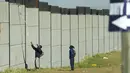 Seorang kolektor besi tua memanjat tembok untuk mencari besi tua untuk didaur ulang di pabrik pengolahan logam di Germiston, timur Johannesburg, Afrika Selatan (30/5/2022). Pengumpul besi tua di area tersebut melompat ke dinding beton untuk mengumpulkan besi tua dan kemudian menjualnya ke toko bekas. (AP Photo/Themba Hadebe)