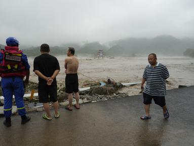 Seorang pekerja penyelamat dan warga lainnya melihat ke arah sungai yang meluap di daerah Miaofengshan di pinggiran Beijing, Selasa, 1 Agustus 2023. (AP Photo/Ng Han Guan)