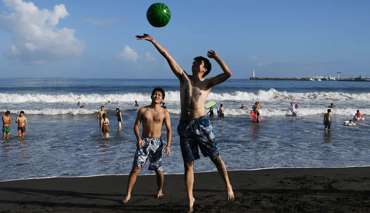 Dua bermain bola berbentuk semangka di sepanjang pantai dekat Pulau Enoshima di pantai Prefektur Kanagawa, barat daya Tokyo (13/8/2019). (AFP Photo/Charly Triballeau)