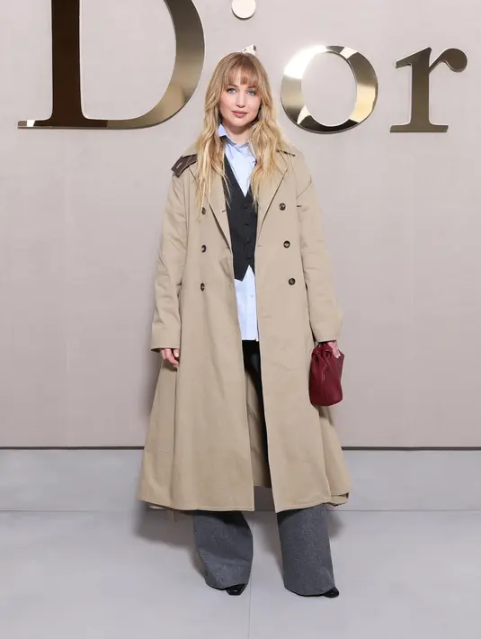 Jennifer Lawrence kenakan outfit layering yang padukan kemeja blue sku dengan vest hitam dan long coat. Baggy jeans hitam jadi sentuhan boyish pada tampilannya [Dior]