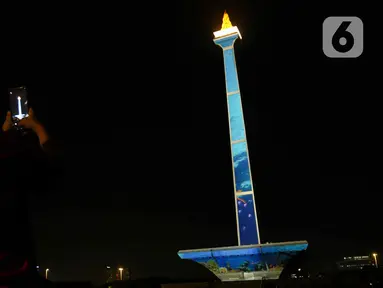 Pengunjung mengambil gambar video mapping dalam Monas Week 2023 di tugu Monumen Nasional (Monas), Jakarta Pusat, Jumat (29/12/2023). (Liputan6.com/Herman Zakharia)