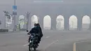 Pengendara sepeda motor melintasi jalan di tengah kabut asap pekat di Lahore pada 24 November 2023. (Arif ALI/AFP)