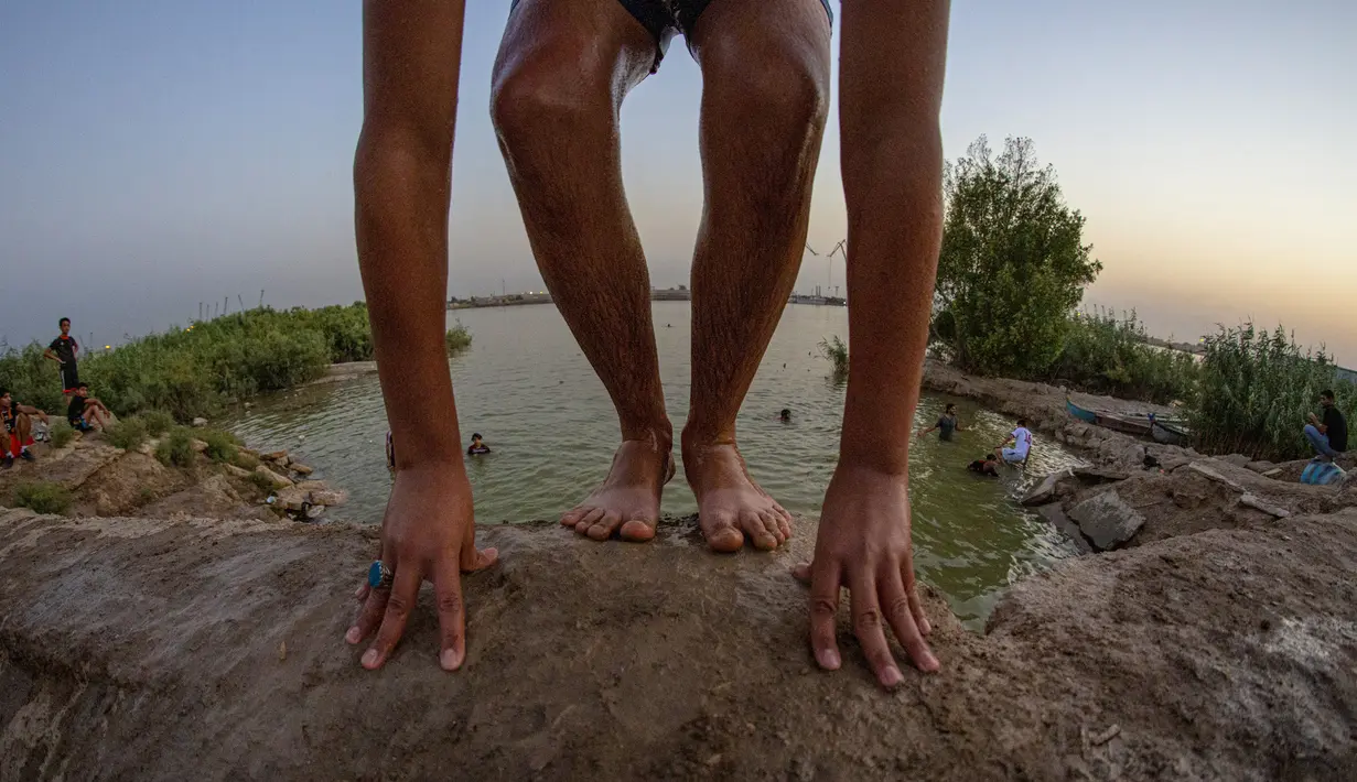 Seorang pemuda bersiap untuk terjun ke Sungai Shatt Al-Arab di Kota Basra, Irak, Selasa (9/6/2020). Sungai yang memiliki panjang sekitar 200 Km ini menandai perbatasan antara Irak dan Iran. (Hussein FALEH/AFP)