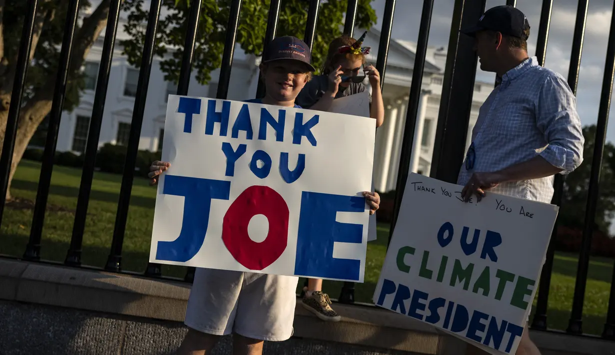 <p>Hugh Kieve (10) memegang papan bertuliskan 'Terima Kasih Joe' bersama saudara perempuannya Margot dan ayahnya David Kieve di sepanjang Pennsylvania Avenue di depan Gedung Putih, Minggu (21/7/2024). (SAMUEL CORUM / AFP)</p>