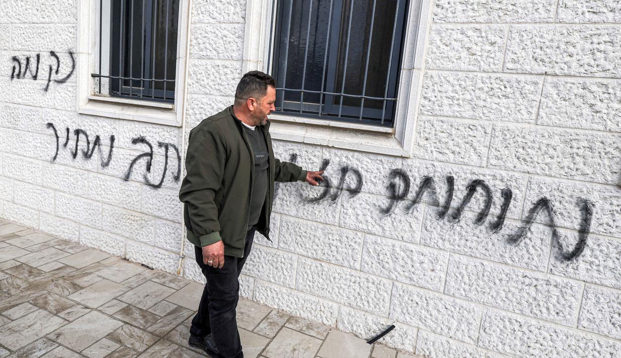 Insiden ini terjadi pada Senin 23 Februari 2026. Tampak dalam foto, seorang pria memeriksa coretan grafiti Ibrani pada dinding luar Masjid Abu Bakr al-Siddiq di desa Tell, sebelah barat Nablus, Tepi Barat yang diduduki, pada 23 Februari 2026. (JAAFAR ASHTIYEH/AFP)