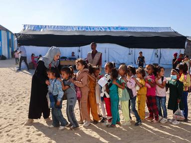 Guru-guru Palestina membariskan murid-murid di halaman sekolah yang didirikan oleh Asosiasi Kebudayaan Mayasem dengan dukungan UNICEF, sebelum pelajaran di kamp pengungsian di kawasan al-Qarara, Khan Yunis, di bagian selatan Jalur Gaza pada Selasa 7 Oktober 2025. (Omar AL-QATTAA/AFP)