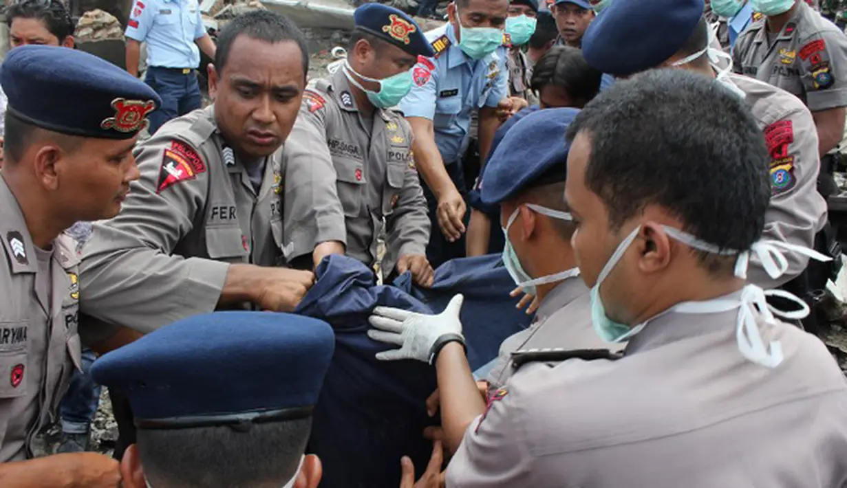 Petugas kepolisian mengevakuasi korban jatuhnya pesawat Hercules C-130 yang jatuh di kawasan perumahan di Medan, Selasa (30/6/2015). Hercules C-130 milik TNI AU jatuh tidak lama setelah lepas landas. (AFP PHOTO/ATAR)