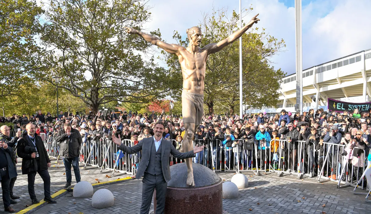 Pesepak bola Zlatan Ibrahimovic berpose di sebelah patung dirinya di Malmo, Swedia, Selasa (8/10/2019). Patung Ibrahimovic mengalami beberapa kali perusakan oleh fans Malmo karena kecewa sang idola membeli saham di klub rival, Hammarby. (Johan NILSSON/TT News Agency/AFP)