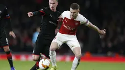 Duel antara Aaron Ramsey dan Benjamin Bourigeaud pada leg kedua,babak 16 besar Liga Europa yang berlangsung di Stadion Emirates, London, Jumat (15/3). Arsenal menang 3-0 atas Rennes. (AFP/Ian Kington)
