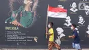 Anak-anak melintas membawa bendera merah putih berlatar belakang mural Pancasila di Kampung Pancasila, Karang Tengah, Kota Tangerang, Selasa (1/6/2021). Sejumlah kegiatan diadakan warga, Komunitas Taman Potret dan TNI ini untuk memperingati Hari kelahiran Pancasila. (Liputan6.com/Angga Yuniar)