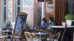 Pengunjung mengenakan masker duduk di kafe di pelabuhan Pulau Poros, Yunani 7/8/2020). Terus bertambahnya jumlah kasus terkonfirmasi coronavirus di beberapa wilayah Yunani memaksa pihak berwenang memberlakukan jam malam pertama selama musim pariwisata di Pulau Poros. (Xinhua/Marios Lolos)