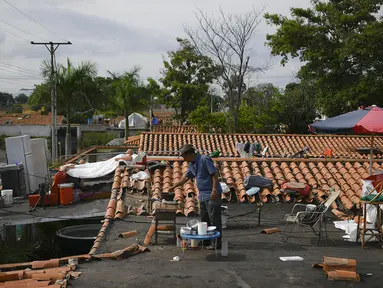 Warga memasak sarapan di atap rumahnya yang banjir di Mata Redonda, Maracay, Venezuela, Rabu (21/10/2020). Hujan deras di negara bagian Aragua menyebabkan Sungai Madre Vieja meluap dan membanjiri beberapa wilayah. (AP Photo/Matias Delacroix)